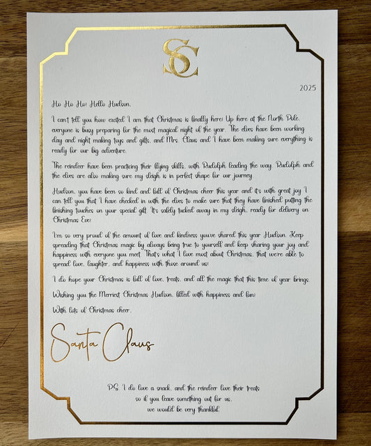 Letter from Santa Claus on a white card with gold border and text, on a wooden surface.
